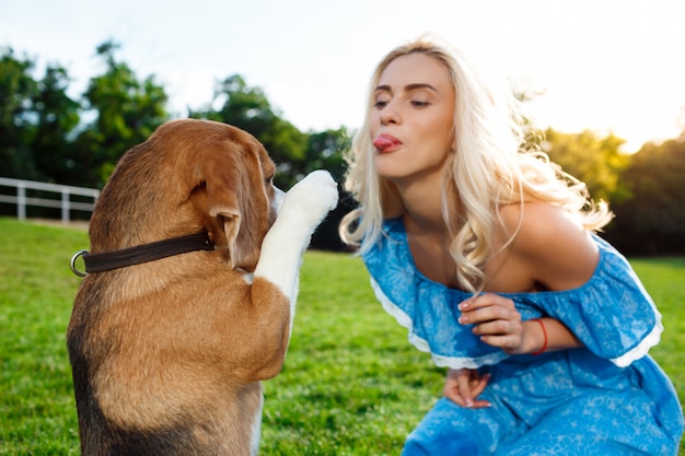 ウォーキング、公園でビーグル犬と遊ぶ若い美しいブロンドの女の子。