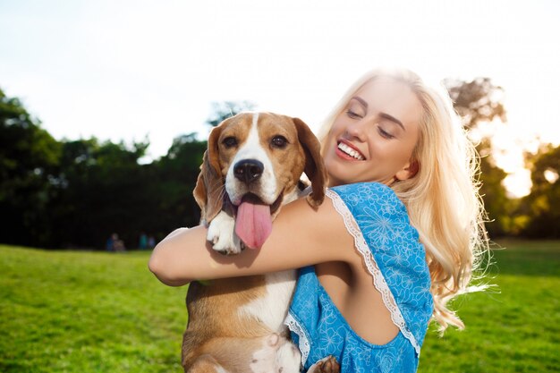 Young beautiful blonde girl walking, playing with beagle dog in park.