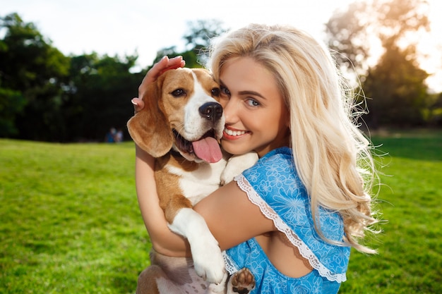 Young beautiful blonde girl walking, playing with beagle dog in park.