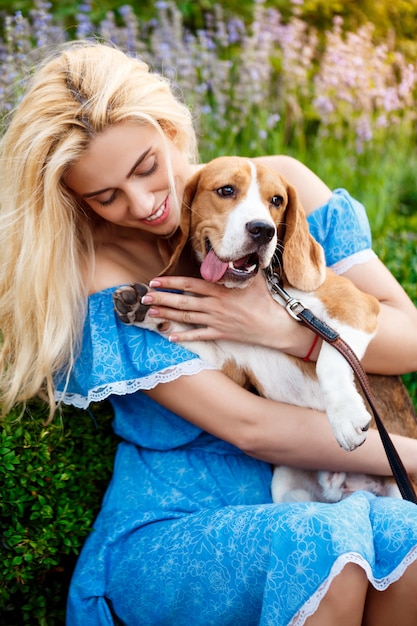 Young beautiful blonde girl walking, playing with beagle dog in park.