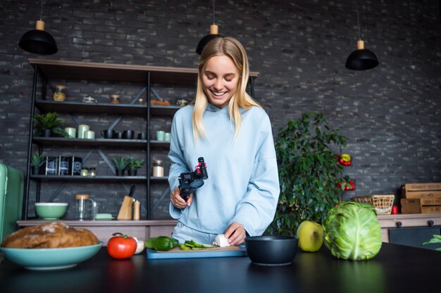 Young beautiful blonde takes on videos as she cooks in the kitchen