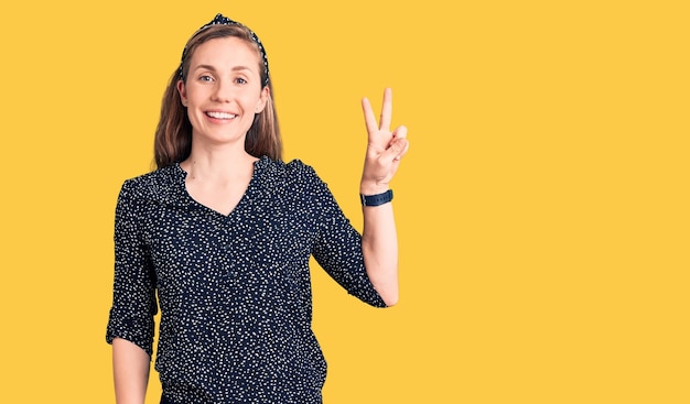 Foto gratuita giovane bella donna bionda che indossa una camicia casual sorridente con la faccia felice che strizza l'occhio alla telecamera facendo il segno di vittoria numero due