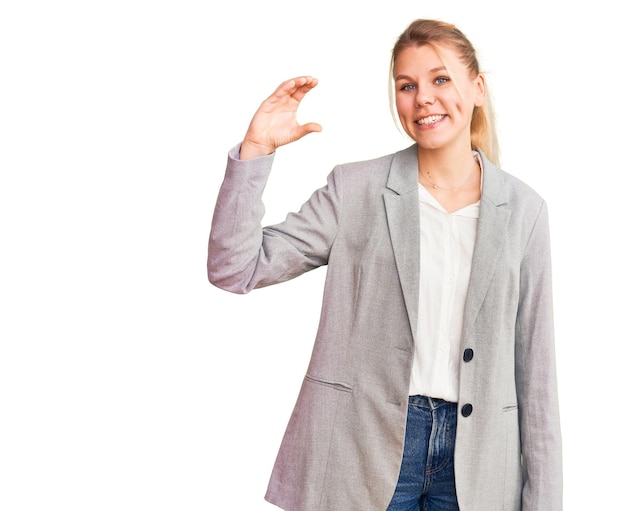 Young beautiful blonde woman wearing elegant jacket smiling and confident gesturing with hand doing small size sign with fingers looking and the camera. measure concept.