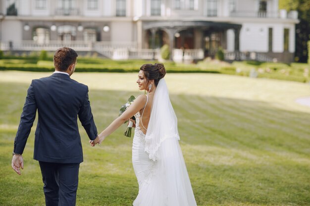 A young and beautiful bride and her husband standing in park with bouquet of flowers