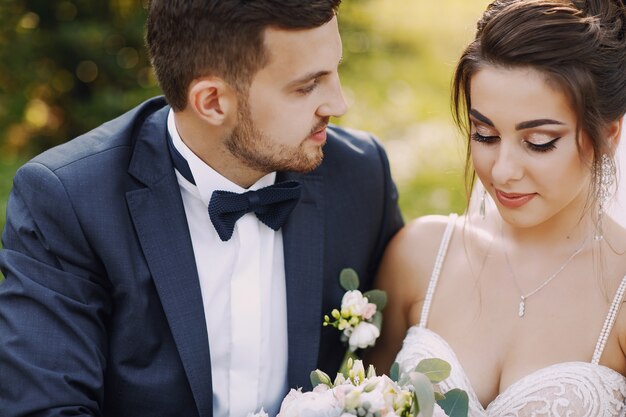 A young and beautiful bride and her husband standing in a park with bouquet of flowers