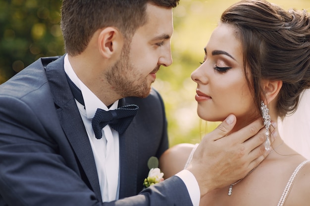 A young and beautiful bride and her husband standing in a park with bouquet of flowers