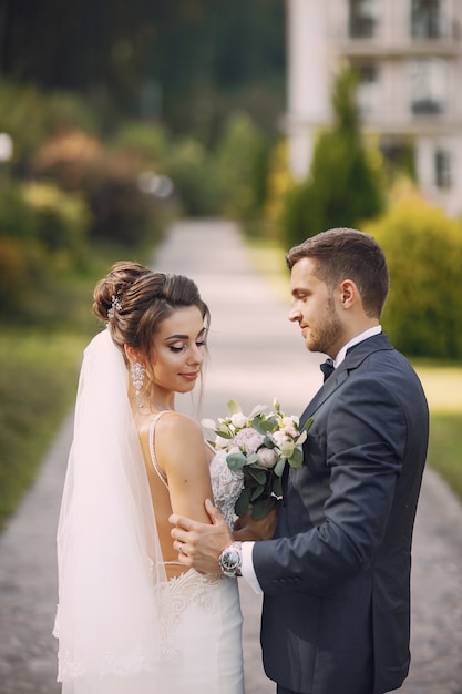 A young and beautiful bride and her husband standing in a park with bouquet of flowers