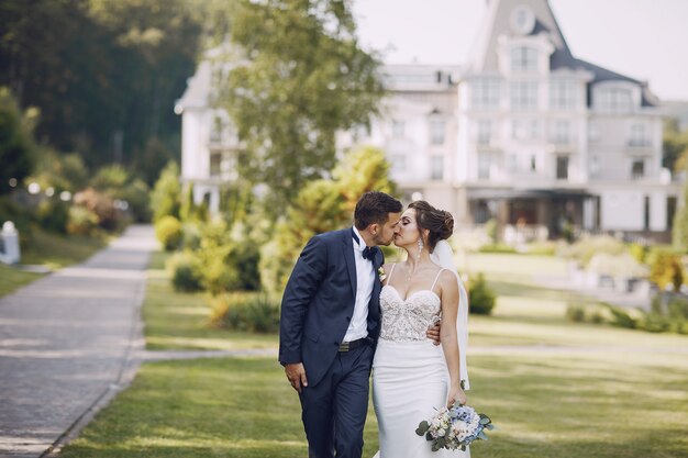 A young and beautiful bride and her husband standing in a summer park with bouquet