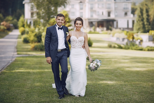 Молодая и красивая невеста и ее муж, стоящая в летнем парке с букетом