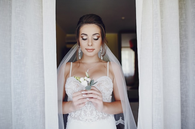 A young and beautiful bride at home standing near window with flowers