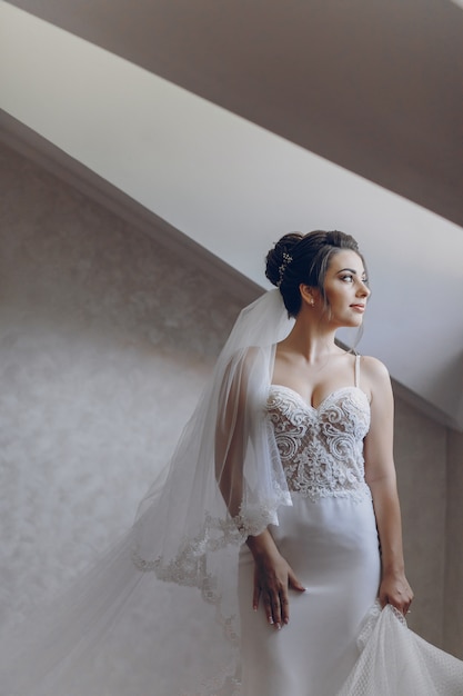 A young and beautiful bride at home standing near window