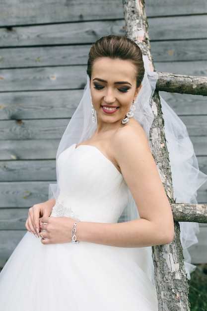 Free photo young beautiful bride standing at the ladder on the background of wooden wall