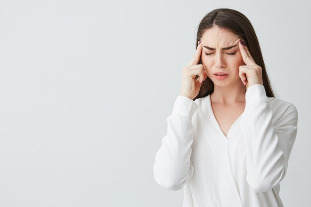 Young beautiful brunette businesswoman holding fingers on temples frowning from pain . Headache.