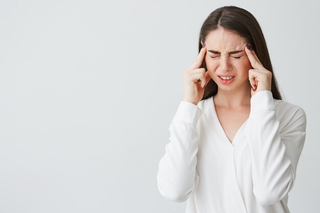 Young beautiful brunette businesswoman holding fingers on temples frowning from pain . Headache.