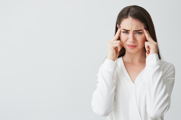 Young beautiful brunette businesswoman holding fingers on temples frowning from pain . Headache.