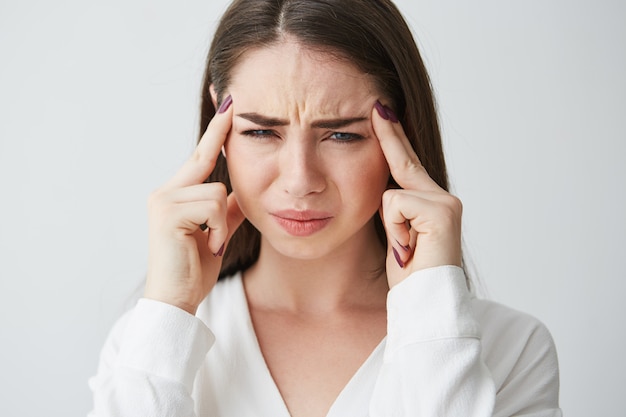 Young beautiful brunette businesswoman holding fingers on temples frowning from pain . Headache.