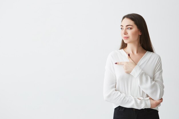 Young beautiful brunette businesswoman smiling looking pointing finger in side .