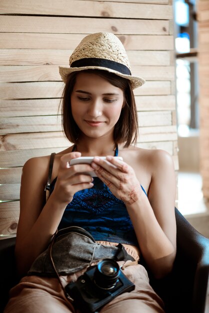 Young beautiful brunette female photographer looking at phone, smiling.