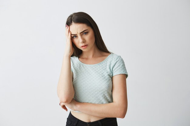 Young beautiful brunette girl frowning touching temple with hand. Headache. Isolated on white background.