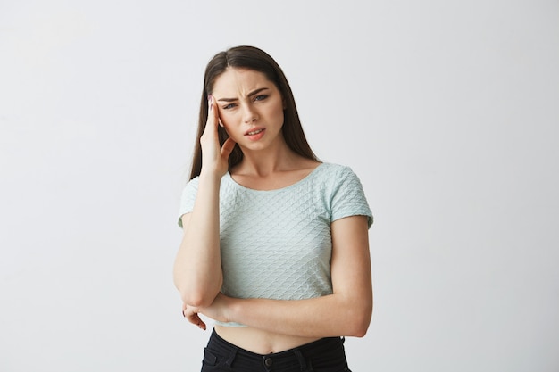 Young beautiful brunette girl frowning touching temple with hand. Headache. Isolated on white background.