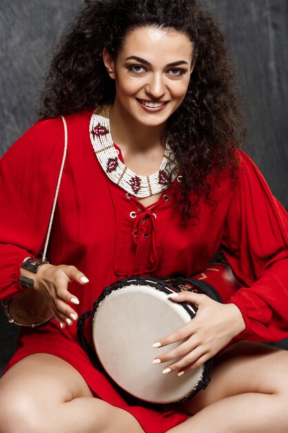 Young beautiful brunette girl playing drum over grey wall