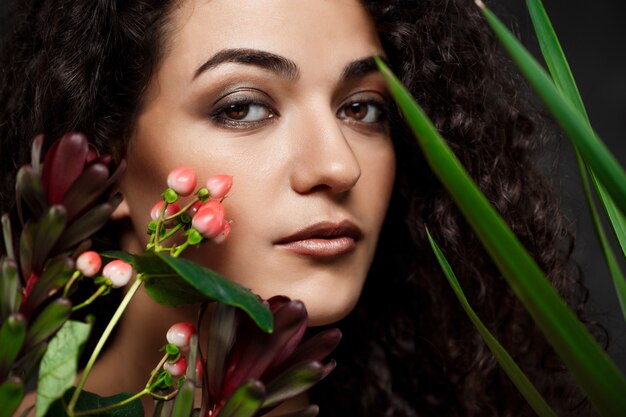 Young beautiful brunette girl in tropical plants over grey wall