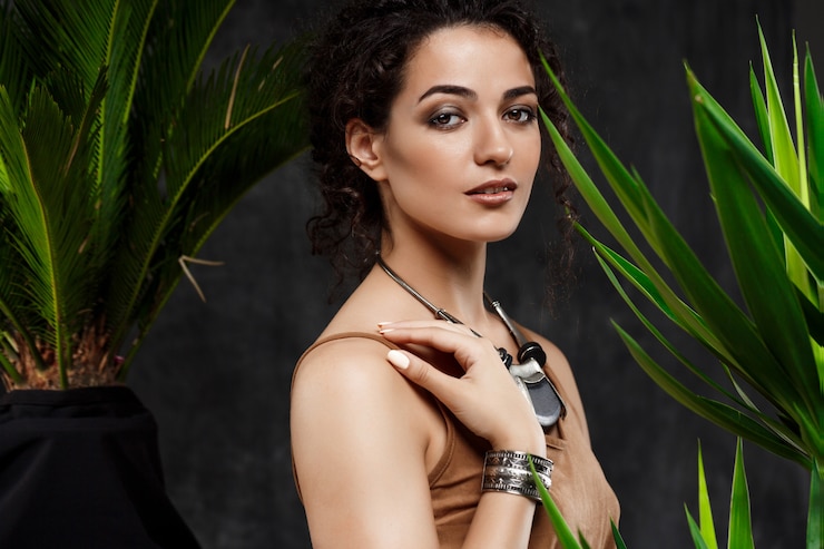 Free Photo young beautiful brunette girl in tropical plants over grey wall
