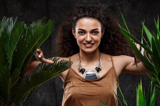 Young beautiful brunette girl in tropical plants over grey wall