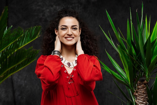 Young beautiful brunette girl in tropical plants over grey wall