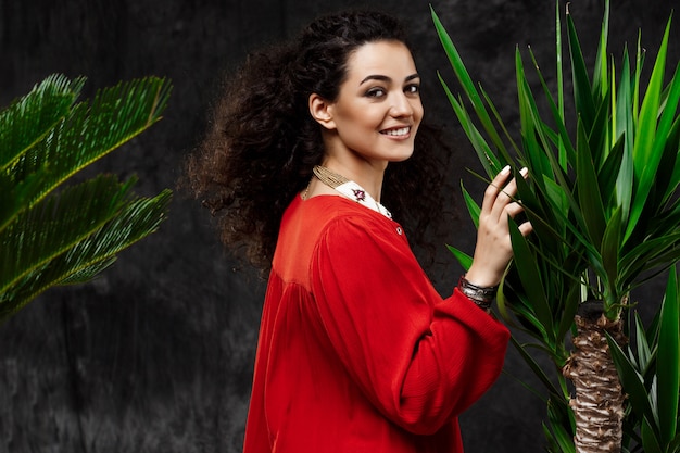 Young beautiful brunette girl in tropical plants over grey wall