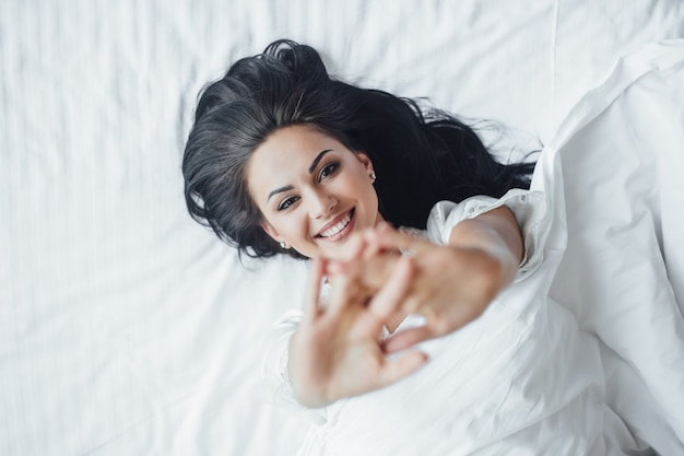 Foto gratuita la giovane bella ragazza bruna felice si trova nel suo letto svegliarsi la mattina e sudare. vista dall'alto.