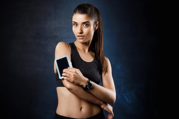 Young beautiful brunette sportive woman posing over dark wall