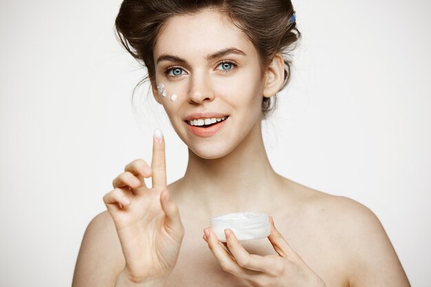 Young beautiful brunette woman in hair curlers smiling creaming face. Facial treatment. Beauty health and cosmetology.