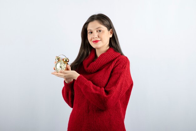 Young beautiful brunette woman holding an alarm clock standing over white background