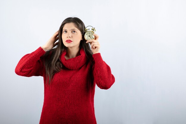 Young beautiful brunette woman holding an alarm clock standing over white background