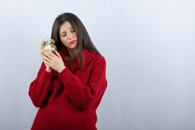 Young beautiful brunette woman holding an alarm clock standing over white background