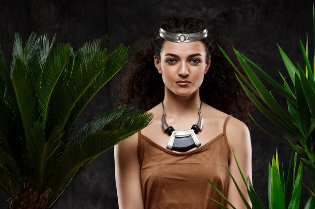 Young beautiful brunette woman in tropical plants over grey wall