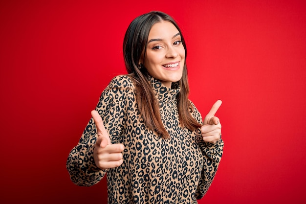 Young beautiful brunette woman wearing casual sweater standing over red background pointing fingers to camera with happy and funny face Good energy and vibes