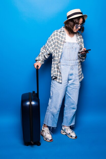 Young beautiful brunette writes text message next to her suitcases isolated