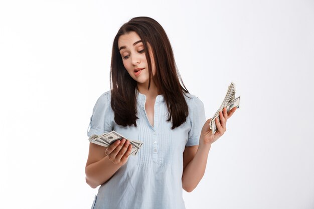 白い壁越しに思慮深くそれらを見てお金を保持している若い美しいビジネス少女