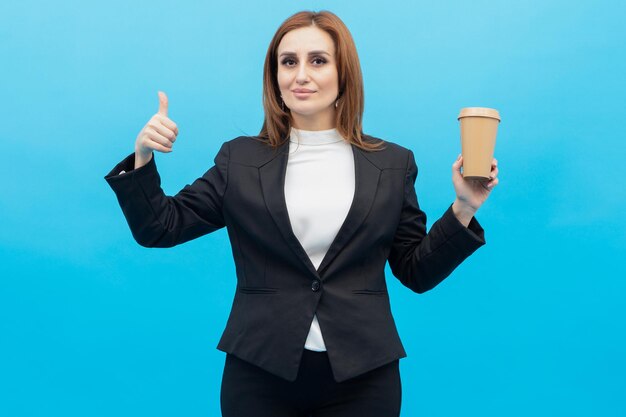 Young beautiful business woman holding coffee cup and gesture thumb up