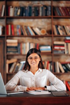 Молодая красивая деловая женщина в очках сидит за рабочим столом