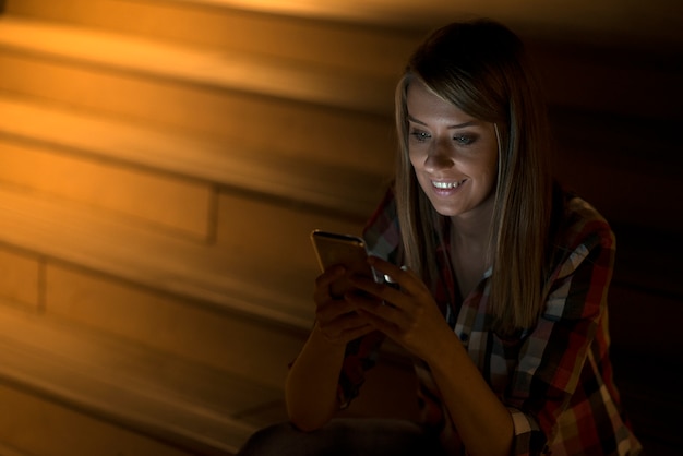 Young beautiful business woman sitting at night lights with mobile smart phone. evening woman working remotely. surfing internet courses, reading books, watching videos online, texting message.