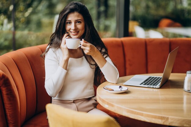 カフェでコンピューターに取り組んでいる若い美しいビジネス女性