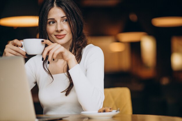 カフェでコンピューターに取り組んでいる若い美しいビジネス女性