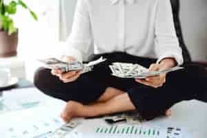 Free photo young beautiful businesswoman holding money, sitting on table at workplace.