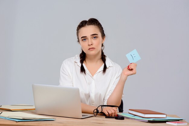 Young beautiful businesswoman sitting at workplace, holding sticker