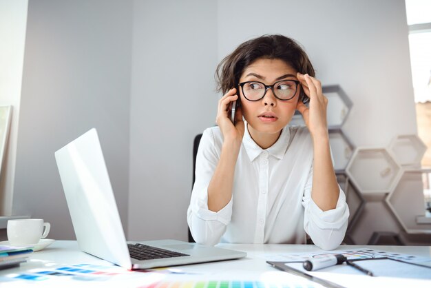 Young beautiful businesswoman speaking on phone at workplace in office. Looking away.