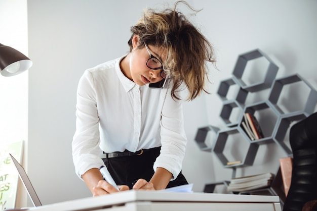 Young beautiful businesswoman with messy hair speaking on phone at workplace in office.