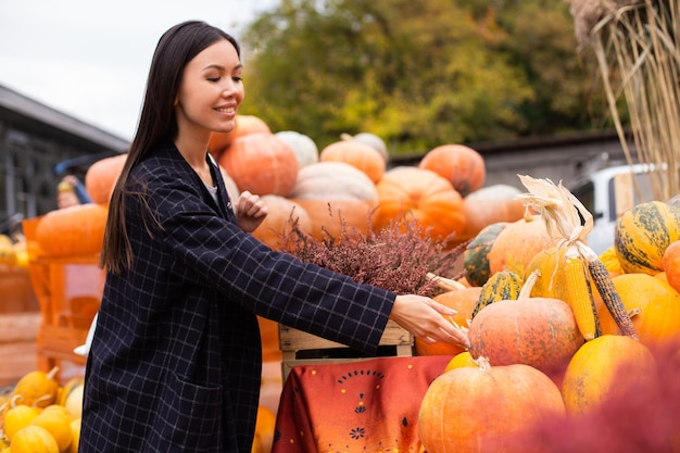 屋外のハロウィーンの日のカボチャを喜んで探している農家の店で若い美しいカジュアルな女性